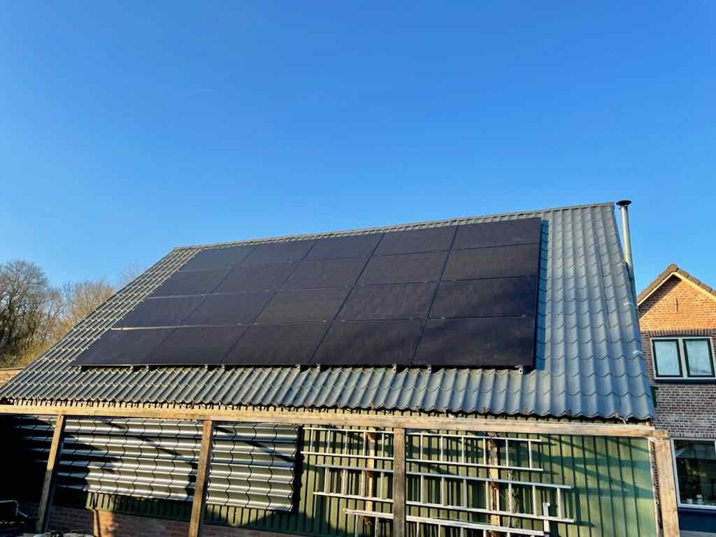 schuurdak met zwarte zonnepanelen tegen een strakblauwe lucht