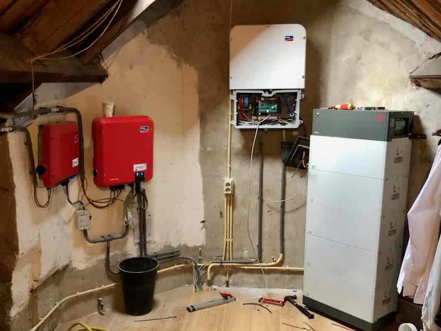 Installatie van een PV systeem met batterijen. De batterij-omvormer (wit) hangt in het midden. Rechts staat de toren van op elkaar gestapelde batterijen