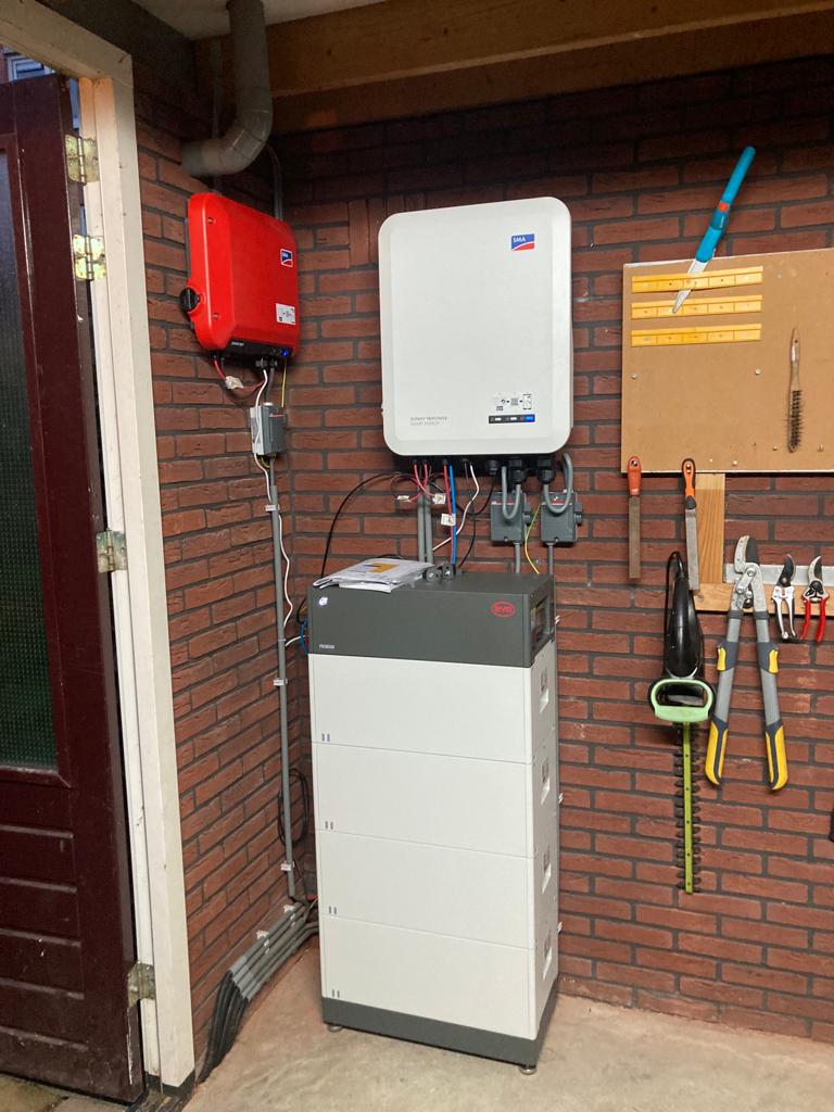 Een thuisbatterij (het grijze apparaat dat op de vloer staat) met een hybride omvormer van SMA (het witte toestel dat daarboven tegen de muur hangt). Hier zullen we nog zeker meer van gaan plaatsen in 2023